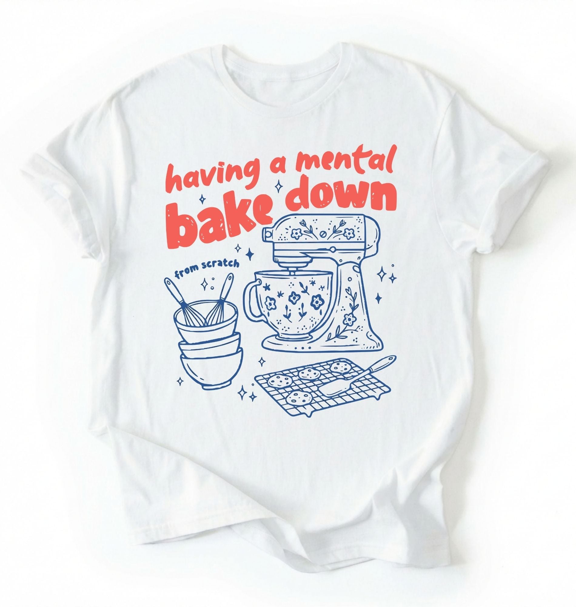 Flat lay of a Having a Mental Bake Down baking shirt with mixer graphic on white t-shirt on a ivory background