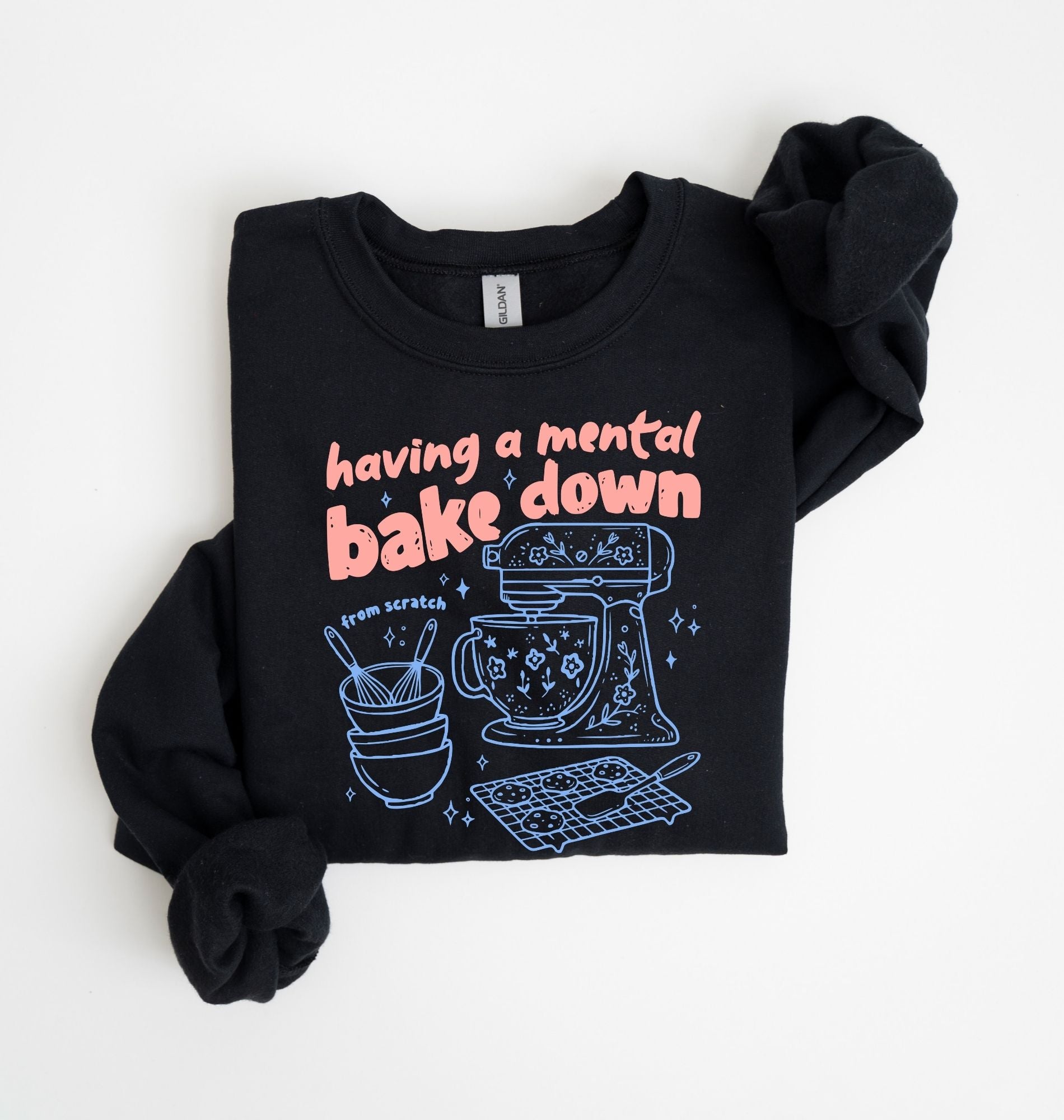 Flat lay of a black Funny Having a Mental Bake Down baking sweatshirt with mixer and baking tools graphic on a white background 