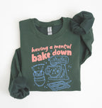 Flat lay of a forest green Funny Having a Mental Bake Down baking sweatshirt with mixer and baking tools graphic on a white background 