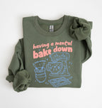 Flat lay of a military green Funny Having a Mental Bake Down baking sweatshirt with mixer and baking tools graphic on a white background 