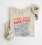 Flat lay of a sand Funny Having a Mental Bake Down baking sweatshirt with mixer and baking tools graphic on a white background 