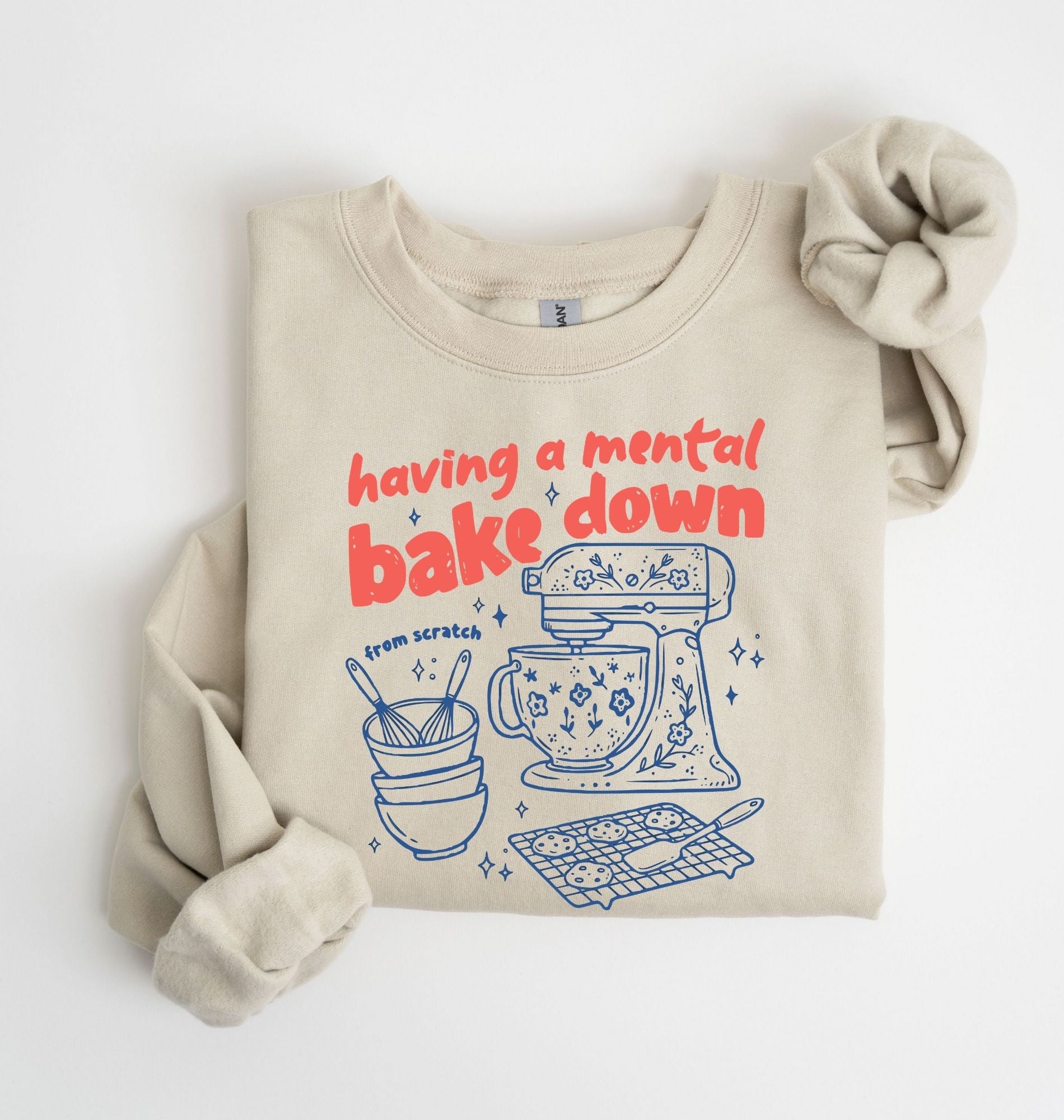 Flat lay of a sand Funny Having a Mental Bake Down baking sweatshirt with mixer and baking tools graphic on a white background 