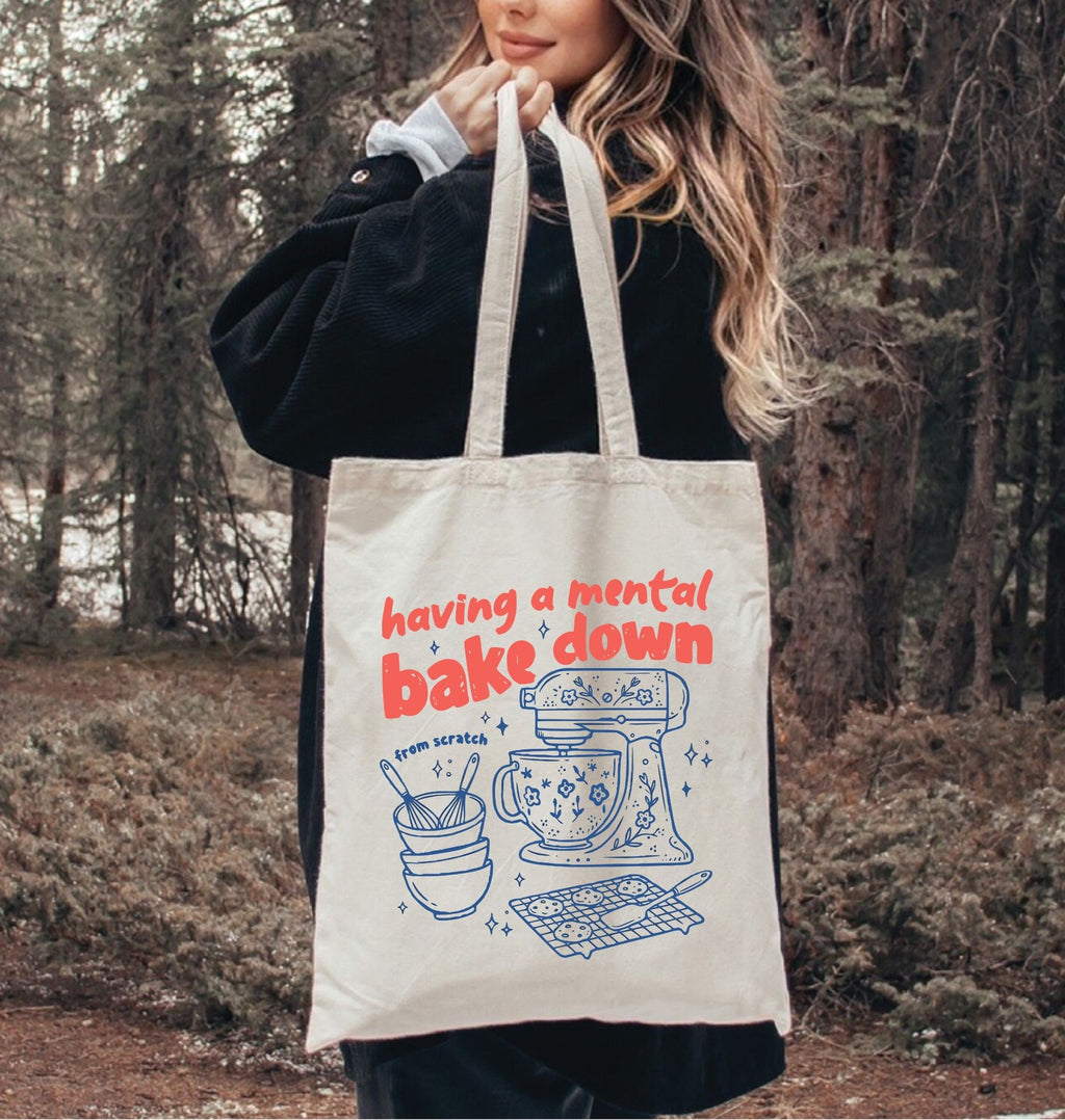 Person holding a tote bag with a humorous kitchen-themed design in a forest setting