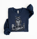 A navy blue sweatshirt with a graphic of a raccoon sitting in a messy bowl of food, with the text 'Having a mental breakdown' printed below it. The sweatshirt is laid flat on a white background with one sleeve folded over.