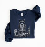 A navy blue sweatshirt with a graphic of a raccoon sitting in a messy bowl of food, with the text 'Having a mental breakdown' printed below it. The sweatshirt is laid flat on a white background with one sleeve folded over.
