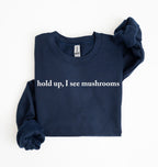 Flat lay of a navyblue-colored sweatshirt on a white background featuring brown text that reads “hold up, I see mushrooms. 