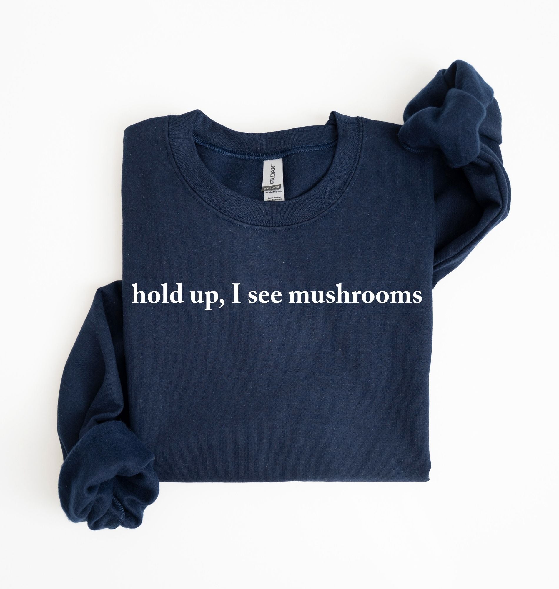 Flat lay of a navyblue-colored sweatshirt on a white background featuring brown text that reads “hold up, I see mushrooms. 