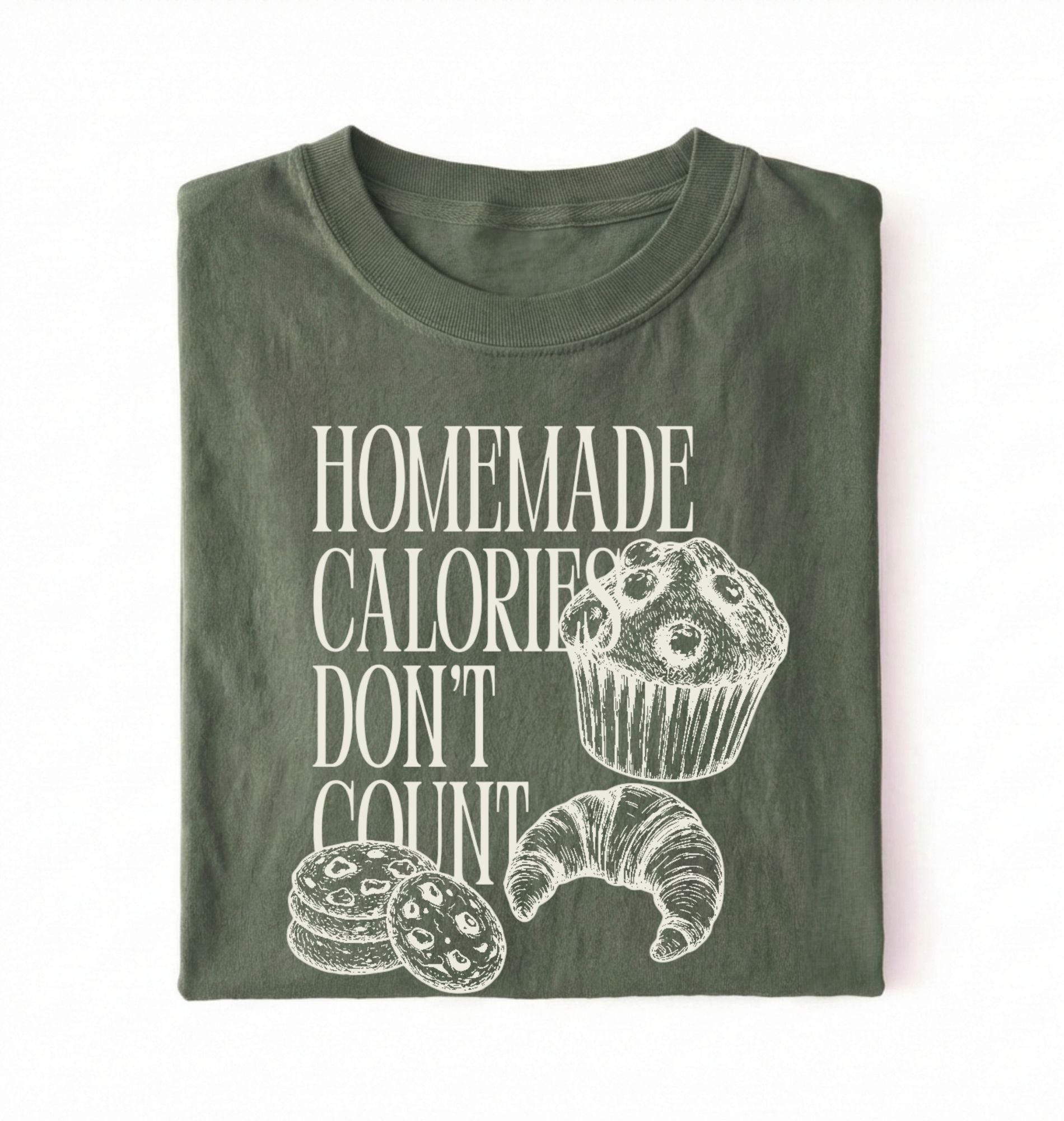 Flat lay of a green Homemade Calories Don't Count baking shirt with muffin cookie and croissant illustrations on a white background 