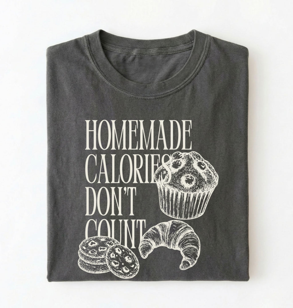 Flat lay of a gray Homemade Calories Don't Count baking shirt with muffin cookie and croissant illustrations on a white background 