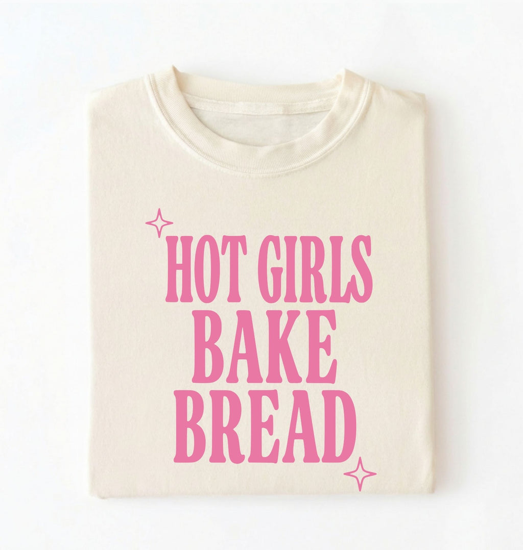 Flat lay of a cream hot girls bake bread shirt with pink text funny sourdough baker gift black t-shirt on a white background 