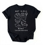 Flat lay of a Funny hot girls bake sourdough shirt with bread and baking tools illustration on black tee on a white background 
