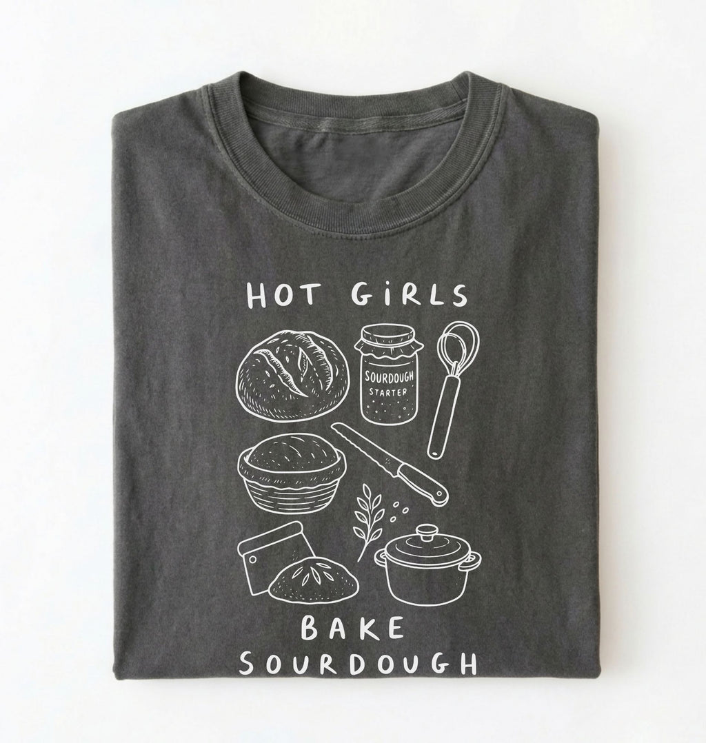 Flat lay of a Funny hot girls bake sourdough shirt with bread and baking tools illustration on pepper tee on a white background 