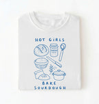 Flat lay of a Funny hot girls bake sourdough shirt with bread and baking tools illustration on white tee on a white background 