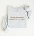 Flat lay of a ash cozy crewneck sweatshirt on a white background with a brown text displaying the phrase “I don’t need more plants (and other lies I tell myself)” centered on the front 