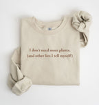 Flat lay of a sand cozy crewneck sweatshirt on a white background with a white text displaying the phrase “I don’t need more plants (and other lies I tell myself)” centered on the front 