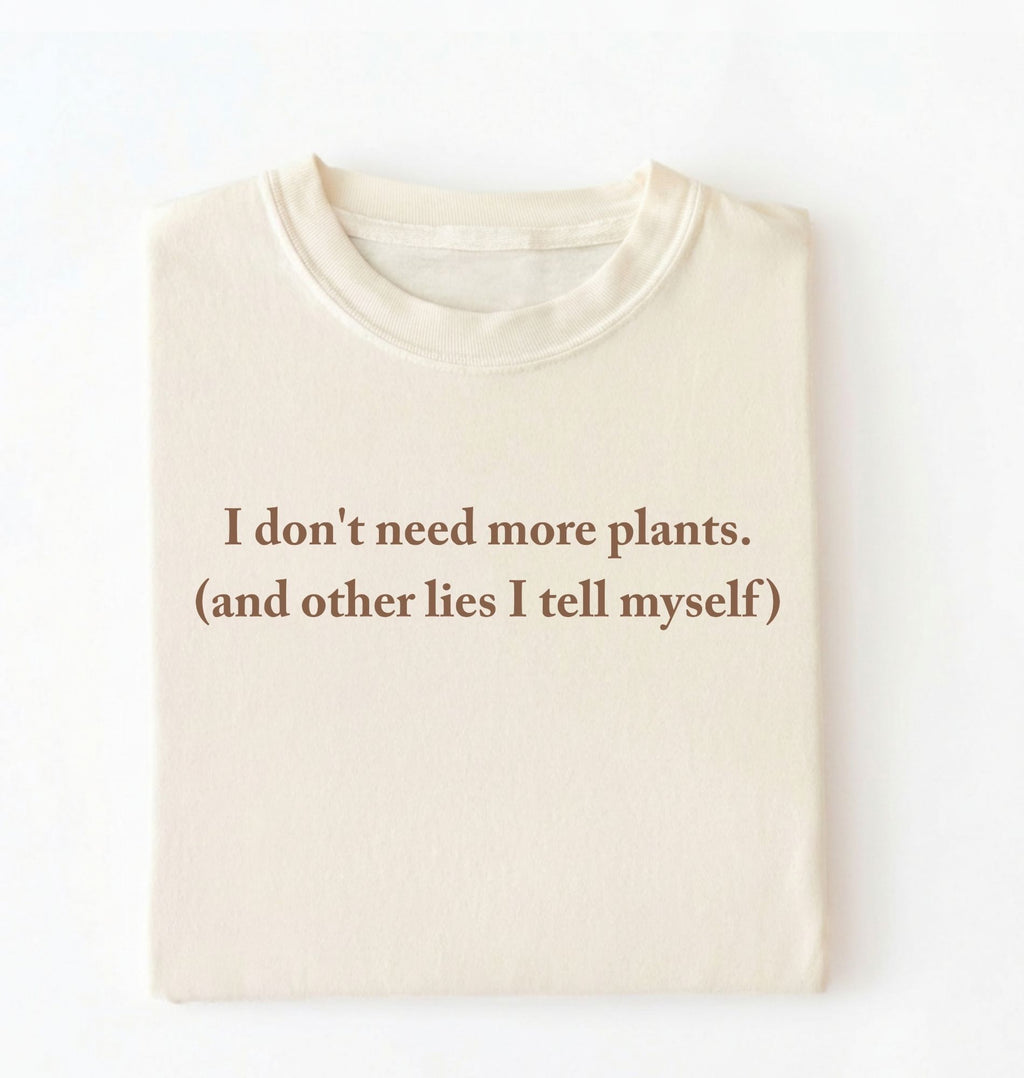 Flat lay of a ivory cozy crewneck t-shirt on a white background with a brown text displaying the phrase “I don’t need more plants (and other lies I tell myself)” centered on the front