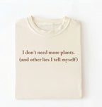 Flat lay of a ivory cozy crewneck t-shirt on a white background with a brown text displaying the phrase “I don’t need more plants (and other lies I tell myself)” centered on the front