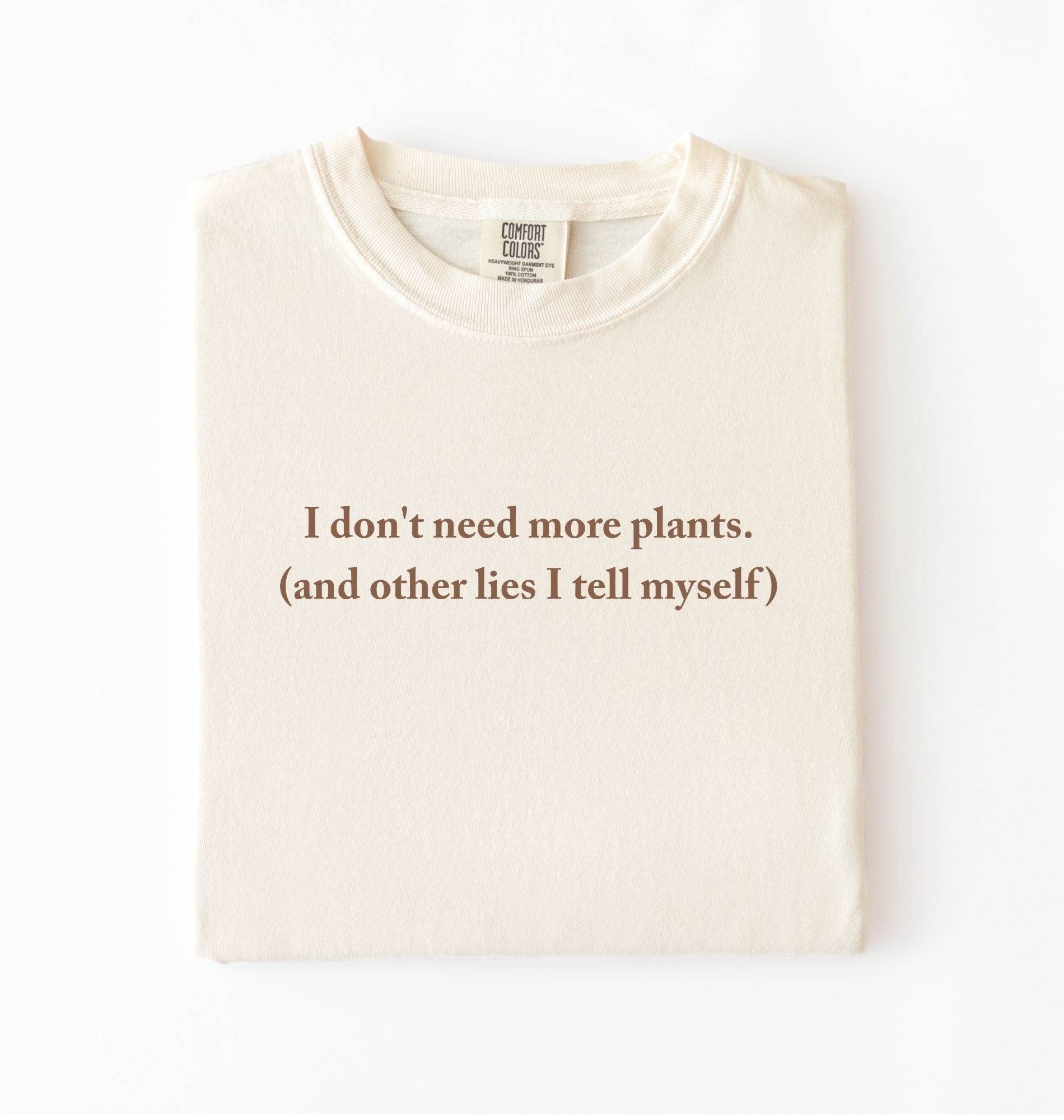Flat lay of a ivory cozy crewneck t-shirt on a white background with a brown text displaying the phrase “I don’t need more plants (and other lies I tell myself)” centered on the front