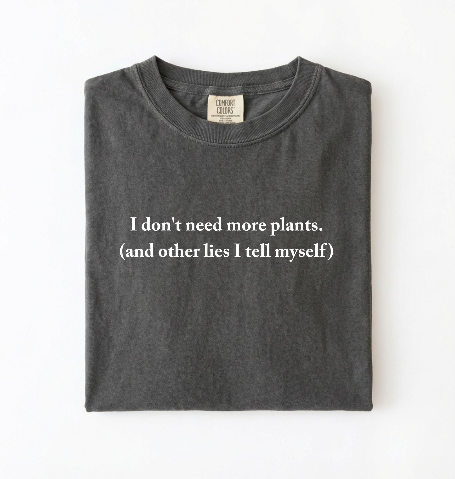Flat lay of a pepper cozy crewneck t-shirt on a white background with a white text displaying the phrase “I don’t need more plants (and other lies I tell myself)” centered on the front