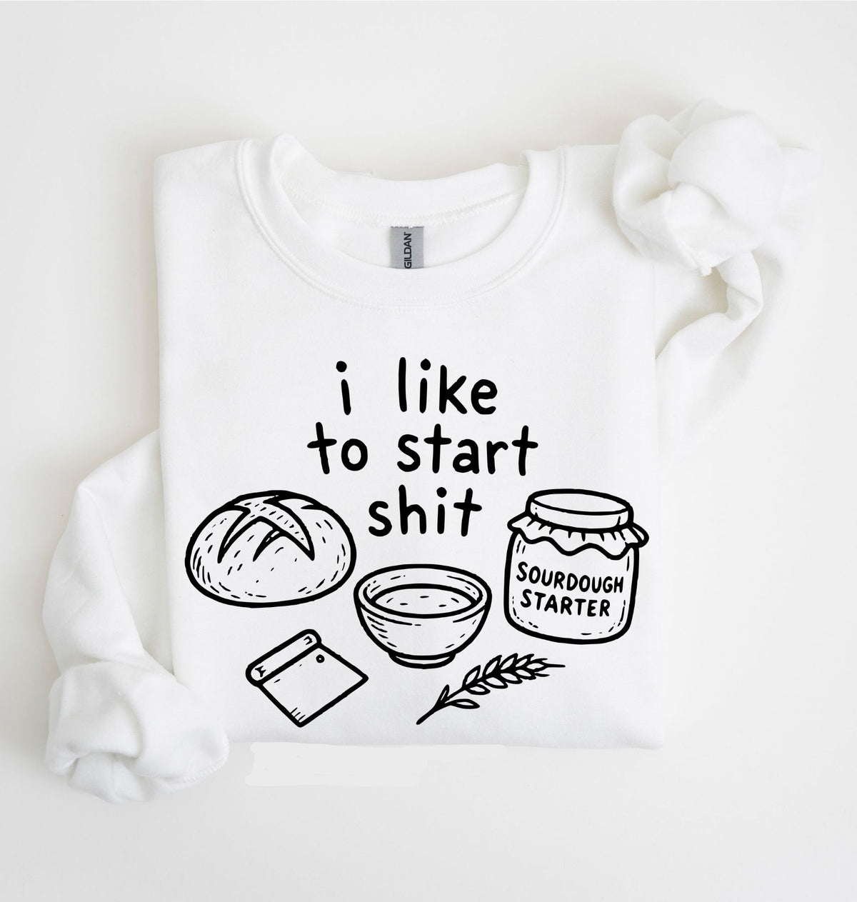 A white long-sleeve crewneck sweatshirt with a black graphic print that reads 'i like to start shit' accompanied by illustrations of a loaf of bread, a bowl, a cutting board, and a jar labeled 'SOURDOUGH STARTER'.