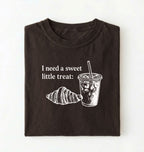 Flat lay of a Cute coffee and croissant shirt with cozy bakery aesthetic on pepper tee on a white background 