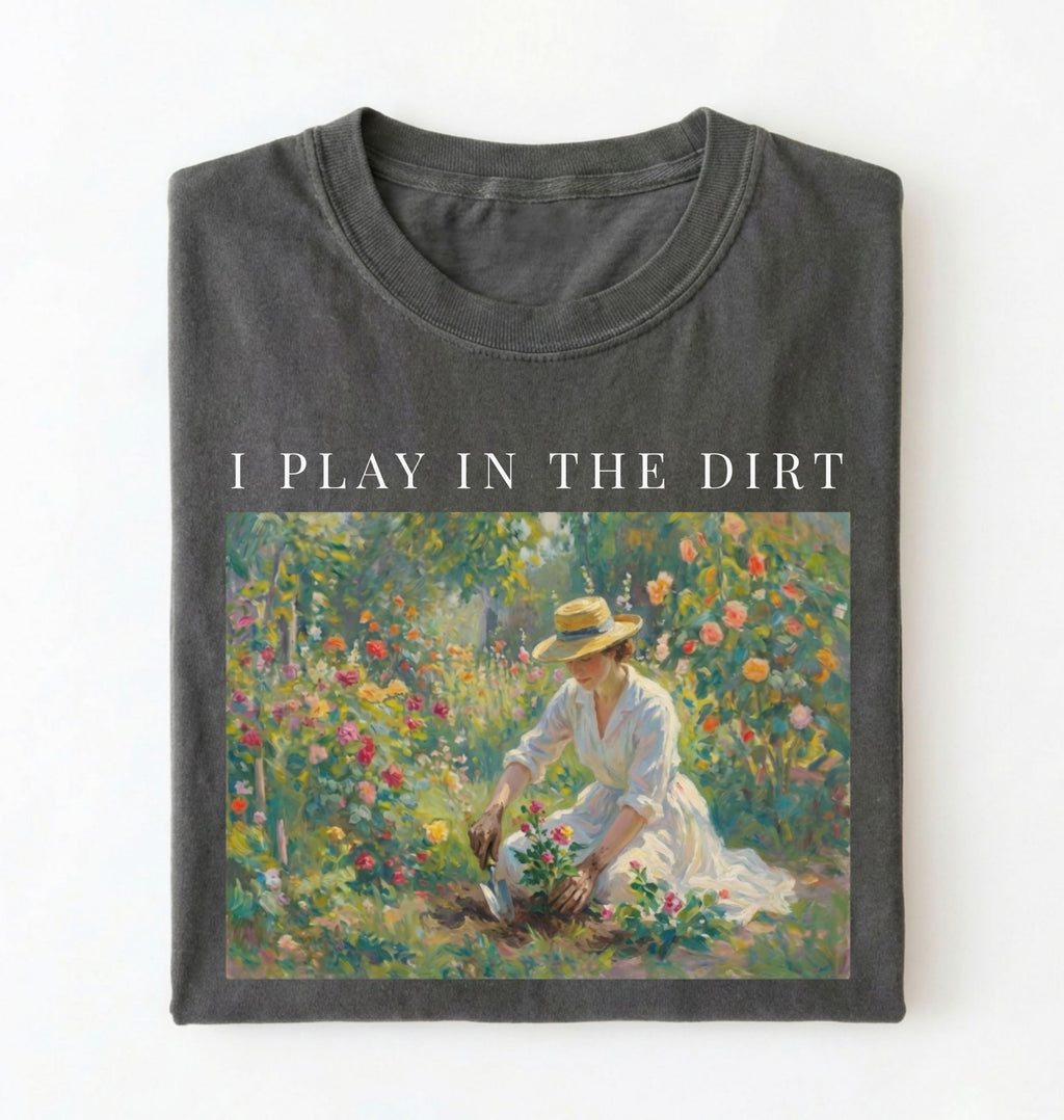 Flat lay of a grey t-shirt featuring a vintage-style garden painting with text reading “I Play In The Dirt.” On a white background 