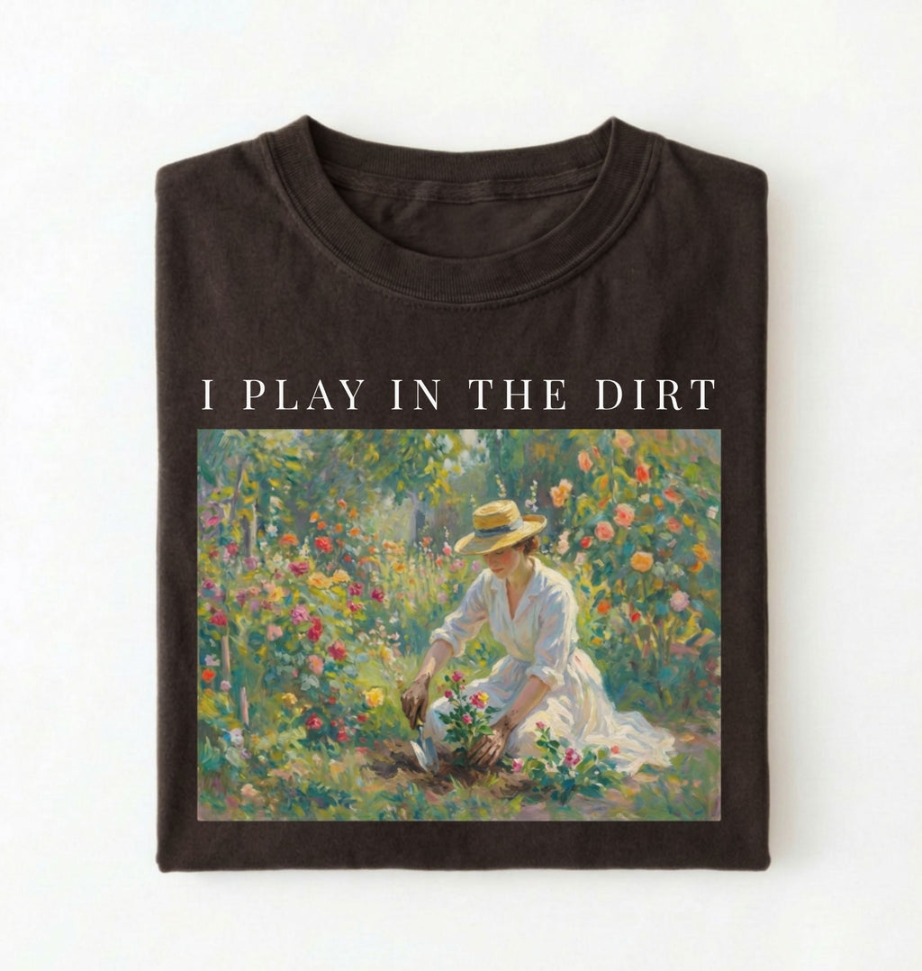 Flat lay of a dark brown chocolate t-shirt featuring a vintage-style garden painting with text reading “I Play In The Dirt.” On a white background 