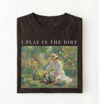 Flat lay of a dark brown chocolate t-shirt featuring a vintage-style garden painting with text reading “I Play In The Dirt.” On a white background 