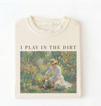 Flat lay of a natural t-shirt featuring a vintage-style garden painting with text reading “I Play In The Dirt.” On a white background 