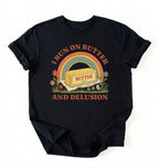 A black short-sleeve t-shirt with a retro-style graphic on the front. The graphic features a rainbow arching over a stick of butter labeled 'BUTTER', with the text 'I RUN ON BUTTER' above and 'AND DELUSION' below in a reddish-brown font, surrounded by small flowers and grass.