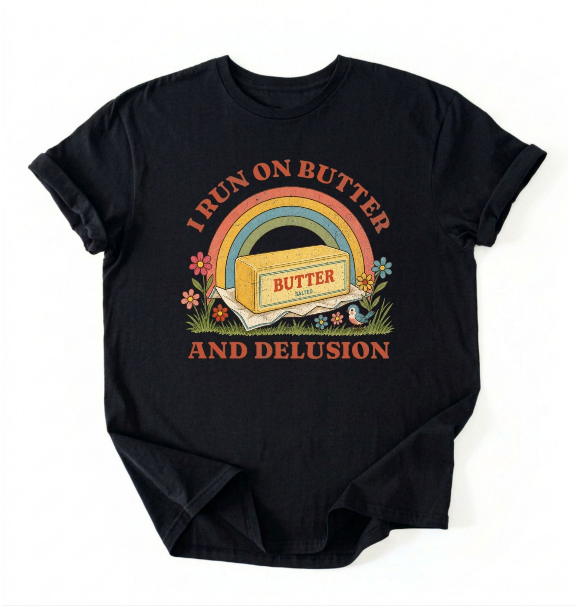 A black short-sleeve t-shirt with a retro-style graphic on the front. The graphic features a rainbow arching over a stick of butter labeled 'BUTTER', with the text 'I RUN ON BUTTER' above and 'AND DELUSION' below in a reddish-brown font, surrounded by small flowers and grass.