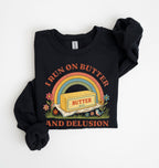 A black long-sleeve sweatshirt with rolled-up sleeves, featuring a retro-style graphic on the front with a rainbow, a butter block labeled 'BUTTER', flowers, and the text 'I RUN ON BUTTER AND DELUSION' on a white  background 