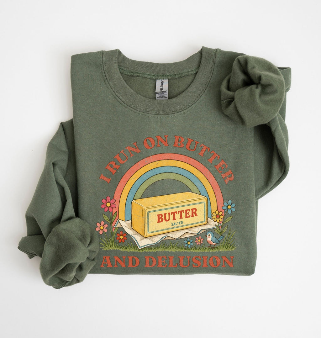 An olive green crewneck sweatshirt with rolled-up sleeves, featuring a retro-style graphic of a butter carton under a rainbow with the text 'I RUN ON BUTTER AND DELUSION' on a white background 