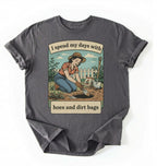 Flat lay of a charcoal Funny gardening shirt with hoes and dirt bags text perfect for gardeners and plant lovers with humor on a white background