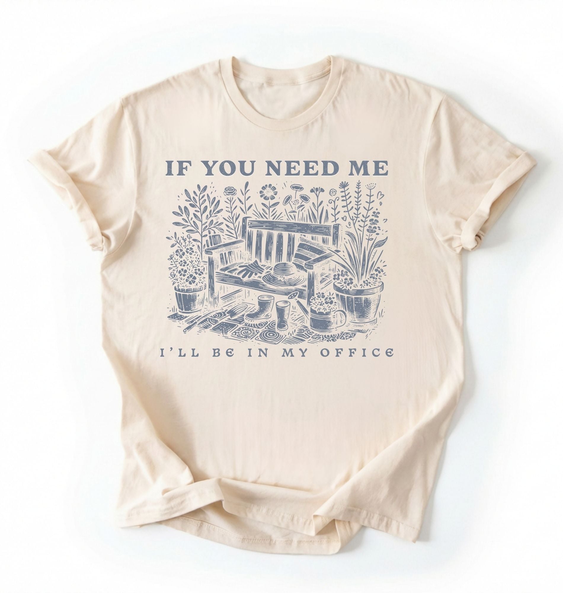 Flat lay of an ivory shirt written "If you need me I’ll be in my office gardening shirt with cottagecore bench and potted plants illustration on a white background 