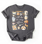Flat lay of a charcoal Baking shirt with tools and desserts saying ill be in my office perfect gift for bakers and home baking lovers on a white background