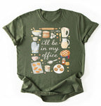 Flat lay of a moss Baking shirt with tools and desserts saying ill be in my office perfect gift for bakers and home baking lovers on a white background