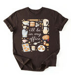 Flat lay of a darkchocolate Baking shirt with tools and desserts saying ill be in my office perfect gift for bakers and home baking lovers on a white background
