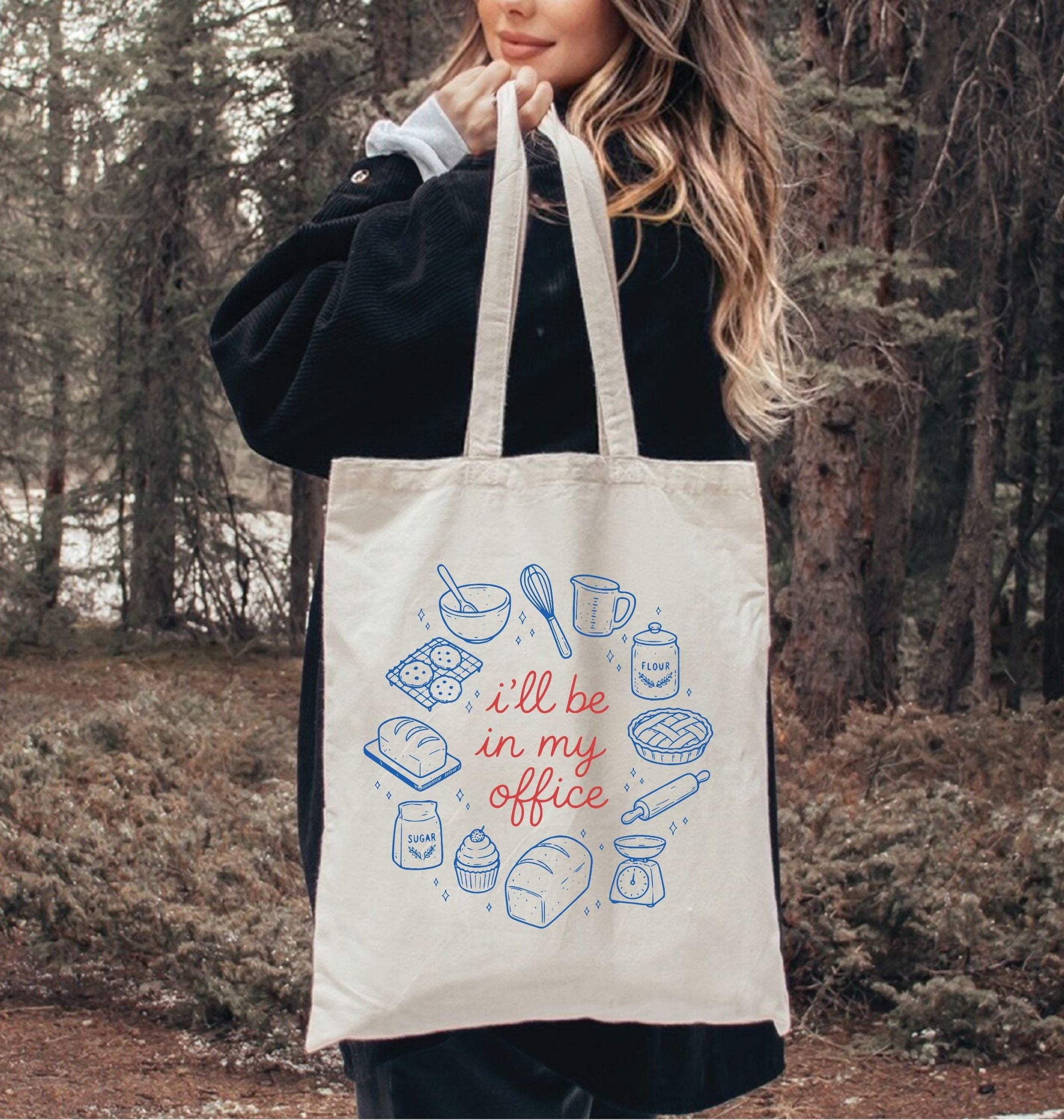 Person holding a tote bag with baking illustrations and text in a forest setting