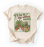 Flat lay of a Natural t-shirt featuring illustrated potted plants, tools, and text reading “I’ll Be In My Office Garden Club on a white background