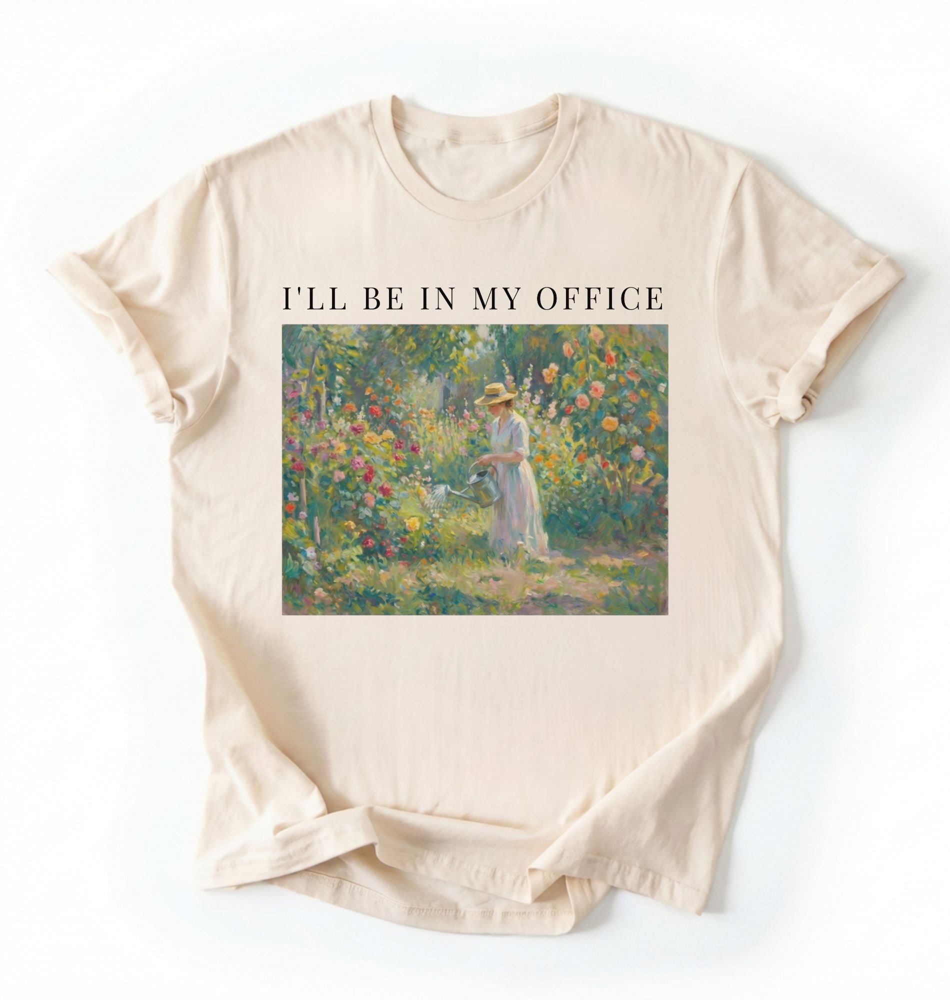 Flat lay of a natural t-shirt featuring a vintage garden painting of a woman tending flowers with text reading “I’ll Be In My Office.” On a white background 