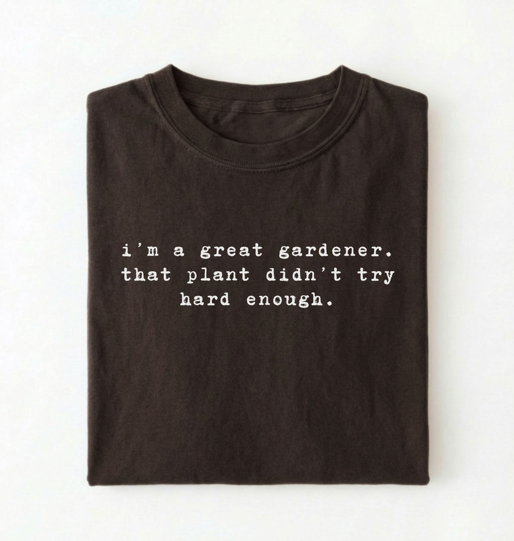 Flat lay of a dark chocolate t-shirt featuring text reading “I’m a great gardener, that plant didn’t try hard enough.” Funny gardening shirt perfect for plant lovers, gardeners and houseplant owners on a white background