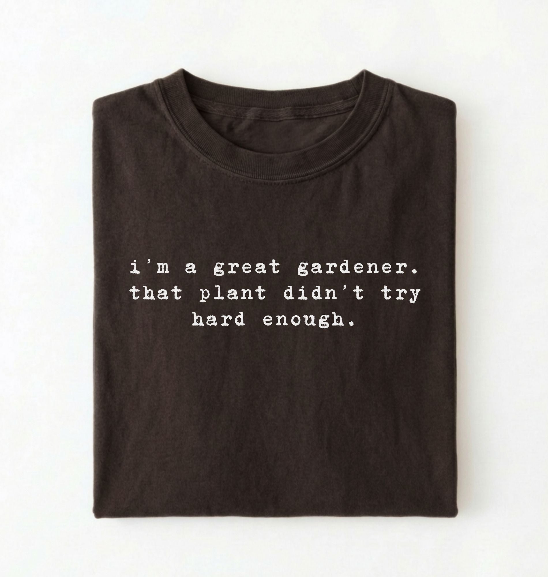 Flat lay of a dark chocolate t-shirt featuring text reading “I’m a great gardener, that plant didn’t try hard enough.” Funny gardening shirt perfect for plant lovers, gardeners and houseplant owners on a white background
