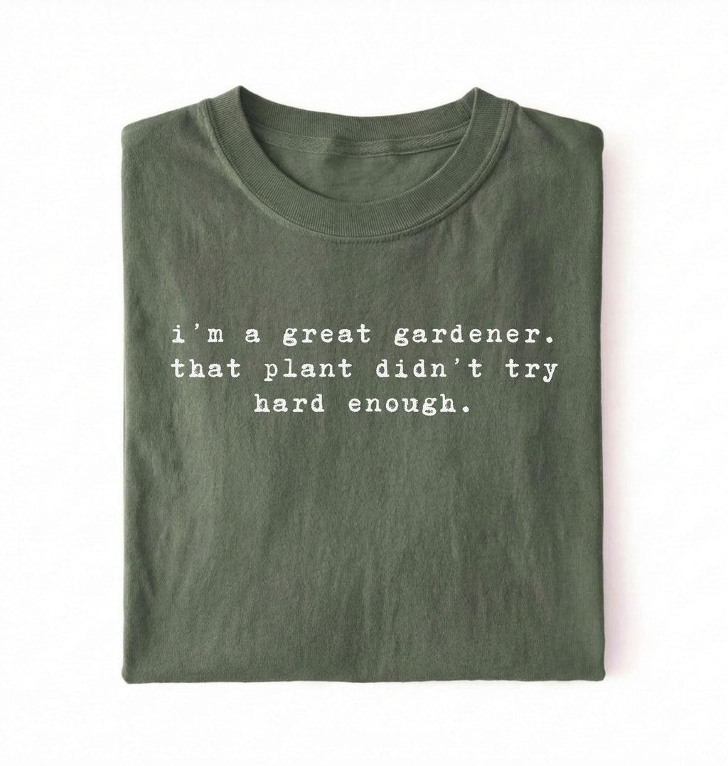 Flat lay of a dark green t-shirt featuring text reading “I’m a great gardener, that plant didn’t try hard enough.” Funny gardening shirt perfect for plant lovers, gardeners and houseplant owners on a white background