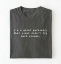 Flat lay of a dark grey t-shirt featuring text reading “I’m a great gardener, that plant didn’t try hard enough.” Funny gardening shirt perfect for plant lovers, gardeners and houseplant owners on a white background