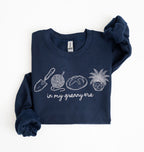 Flat lay of a navy blue crewneck sweatshirt with line drawings of gardening items and text reading “in my granny era.”
