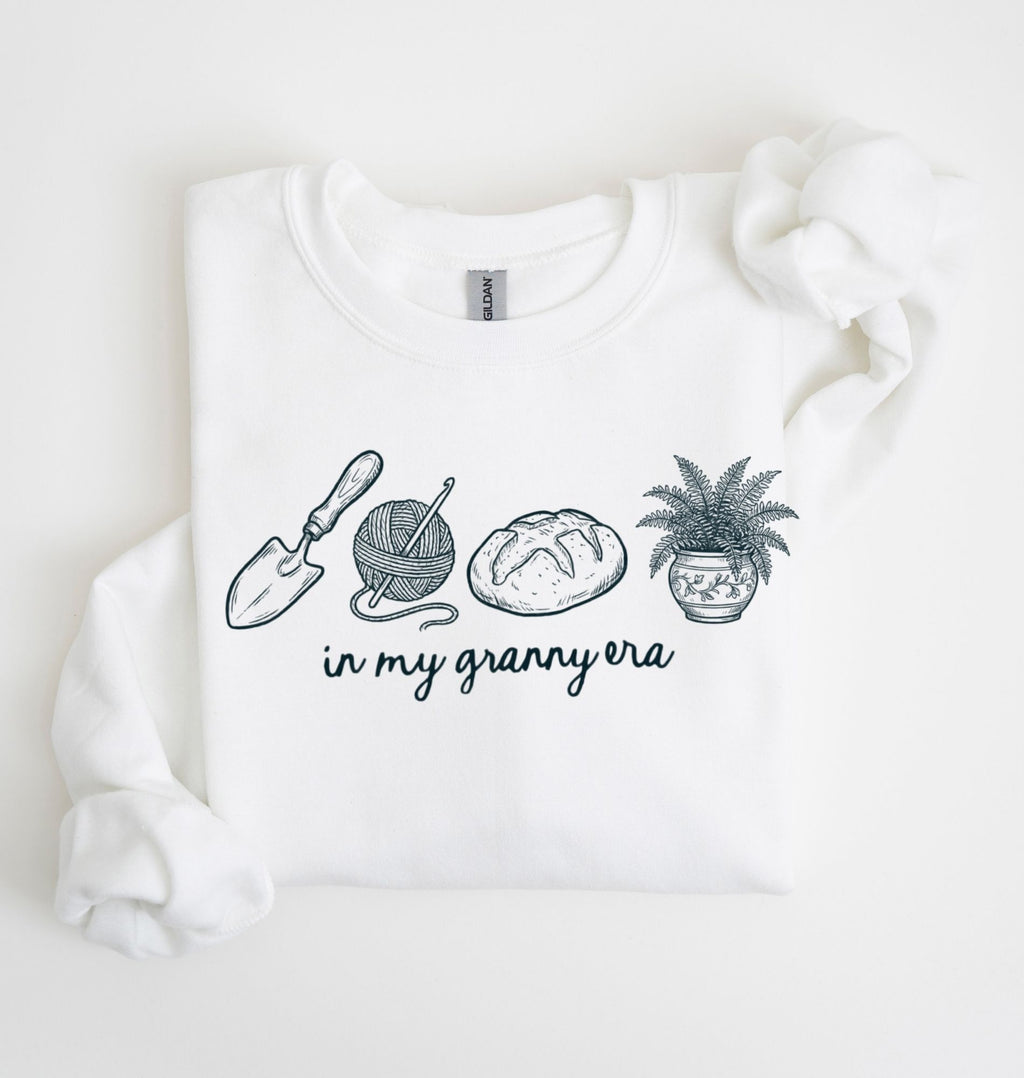Flat lay of a white crewneck sweatshirt with line drawings of gardening items and text reading “in my granny era.”