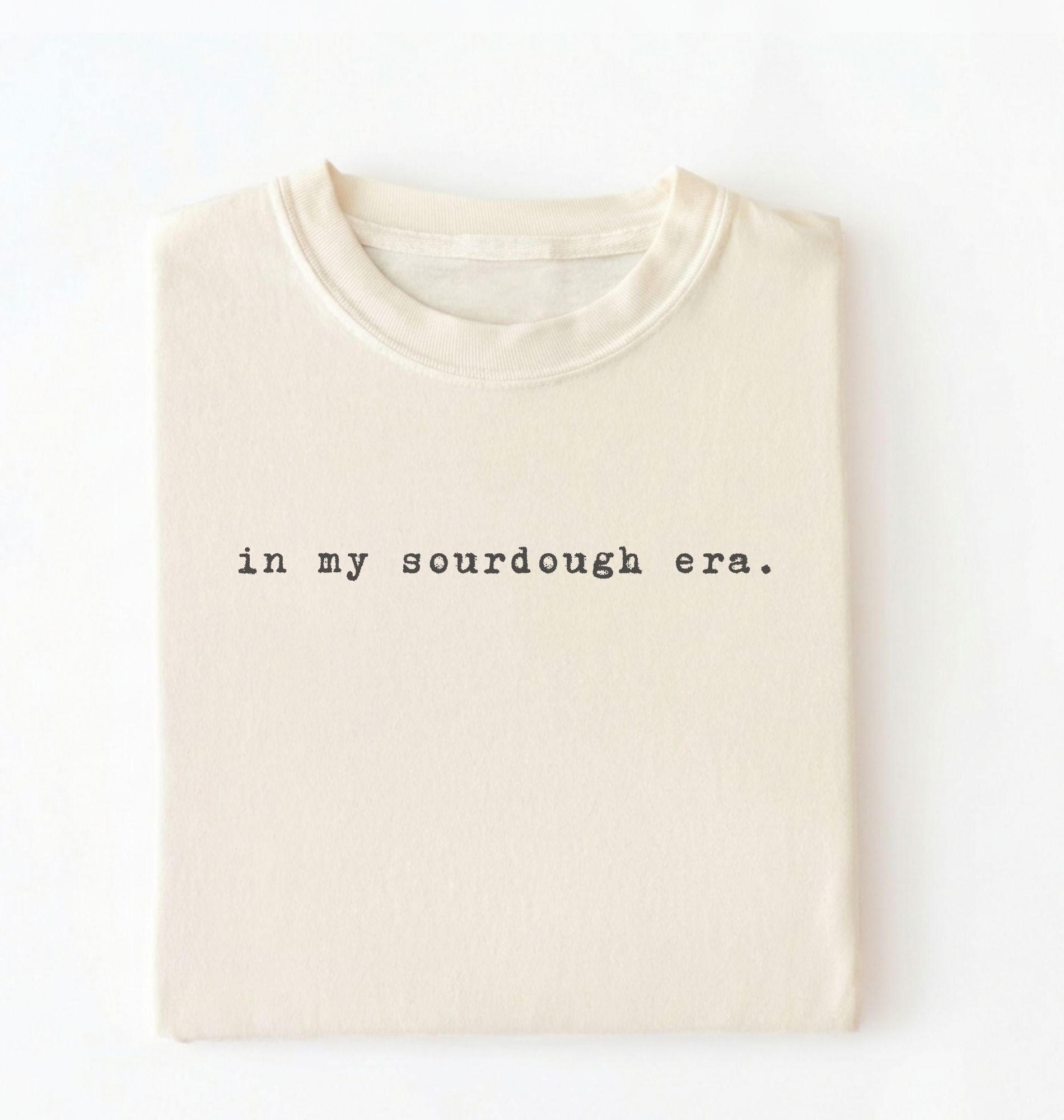 Flat lay of a ivory Funny in my sourdough era baking shirt perfect for bread lovers home bakers and cozy kitchen aesthetic on a white background