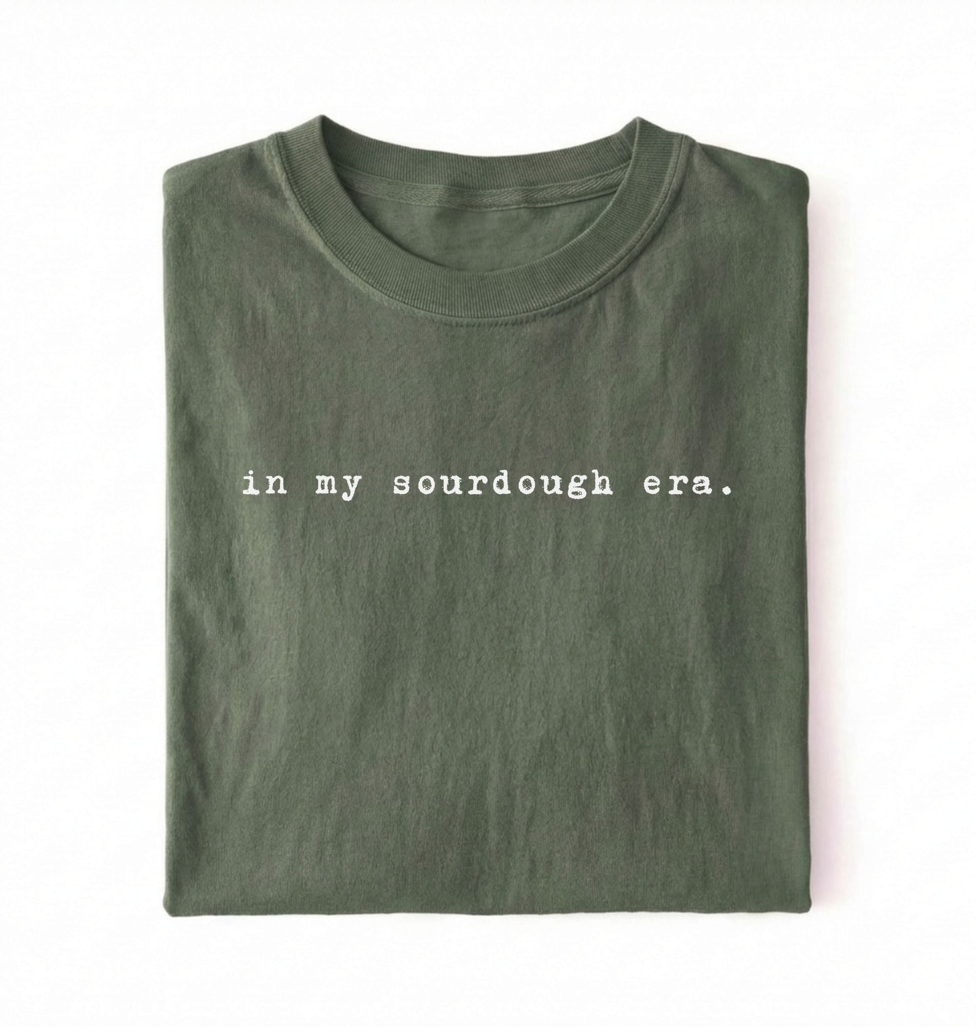 Flat lay of a moss Funny in my sourdough era baking shirt perfect for bread lovers home bakers and cozy kitchen aesthetic on a white background