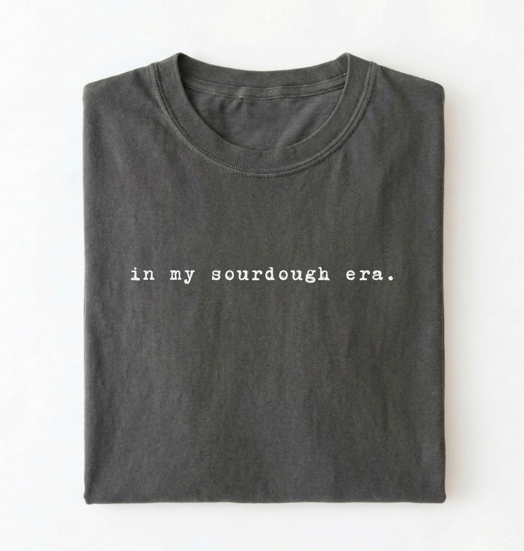 Flat lay of a pepper Funny in my sourdough era baking shirt perfect for bread lovers home bakers and cozy kitchen aesthetic on a white background